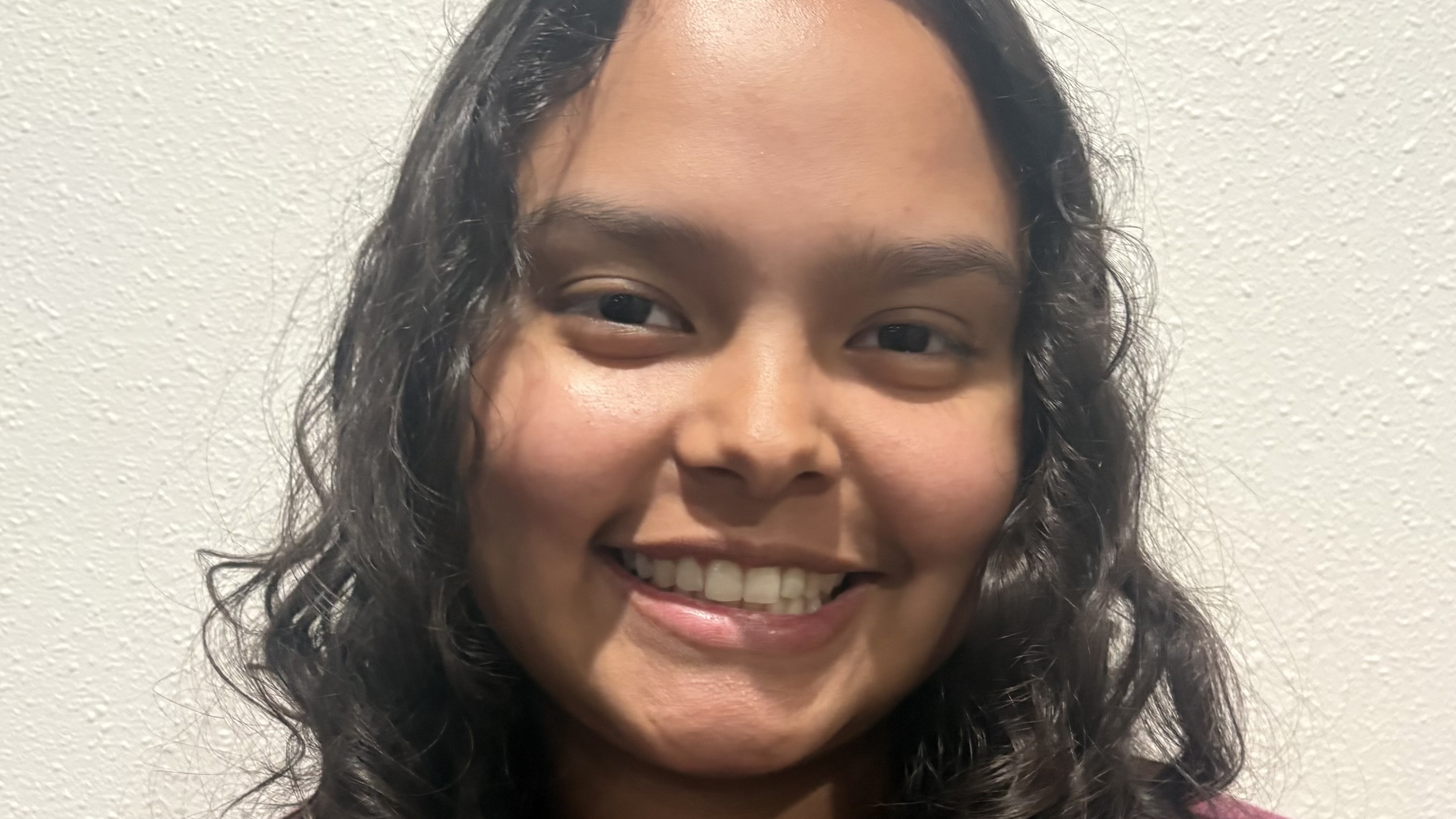 Emalisa Martinez smiles in front of a beige background. Emalisa Martinez smiles in front of a beige background.